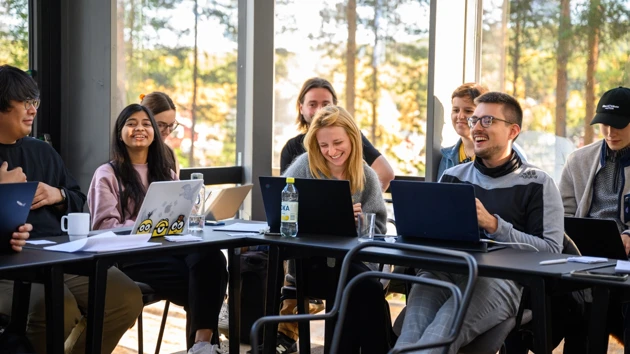 A group of people sitting around a table with laptops