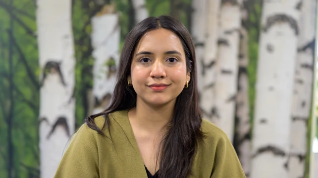 A woman with long dark hair poses in front of a birch tree background